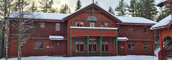 En stor rød trebygning med en grønn balkong er dekket av snø.
